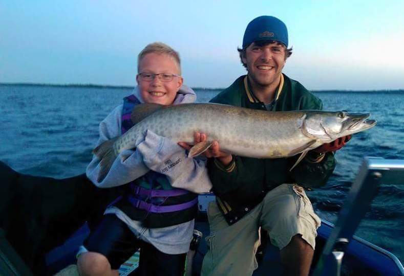 Two gentleman holding up a large muskie they caught during the day on the lake