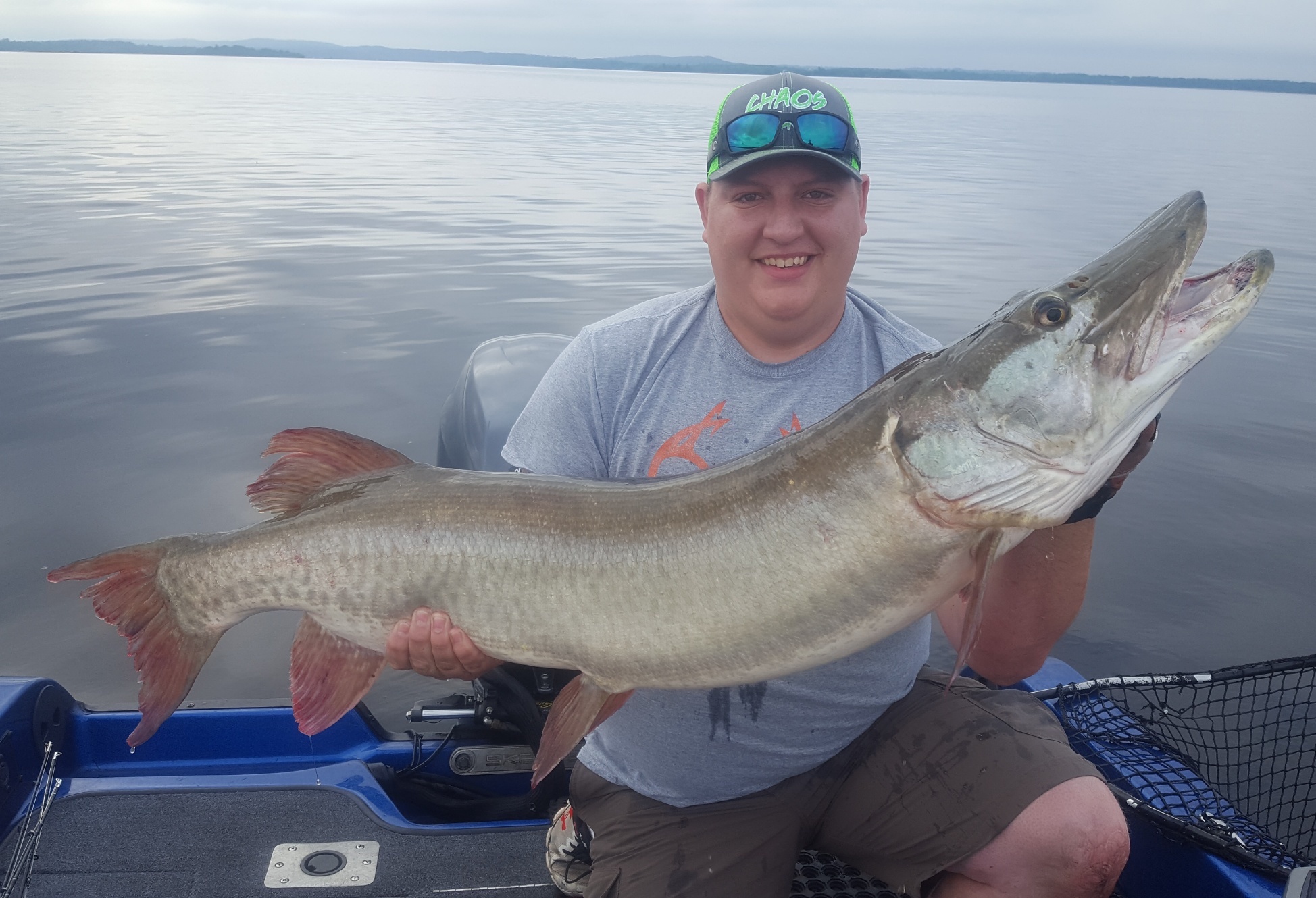 Guy on fishing boat with hat and sunglasses holding a trophy size muskie he caught with Living Legends Guide Service 