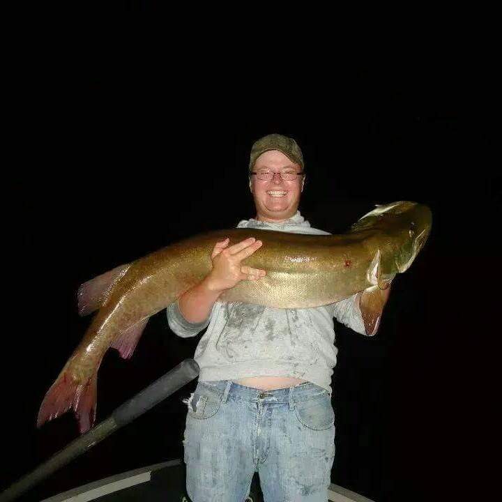 Guy holding a large muskie with both hands while fishing on Lake Vermilion at night