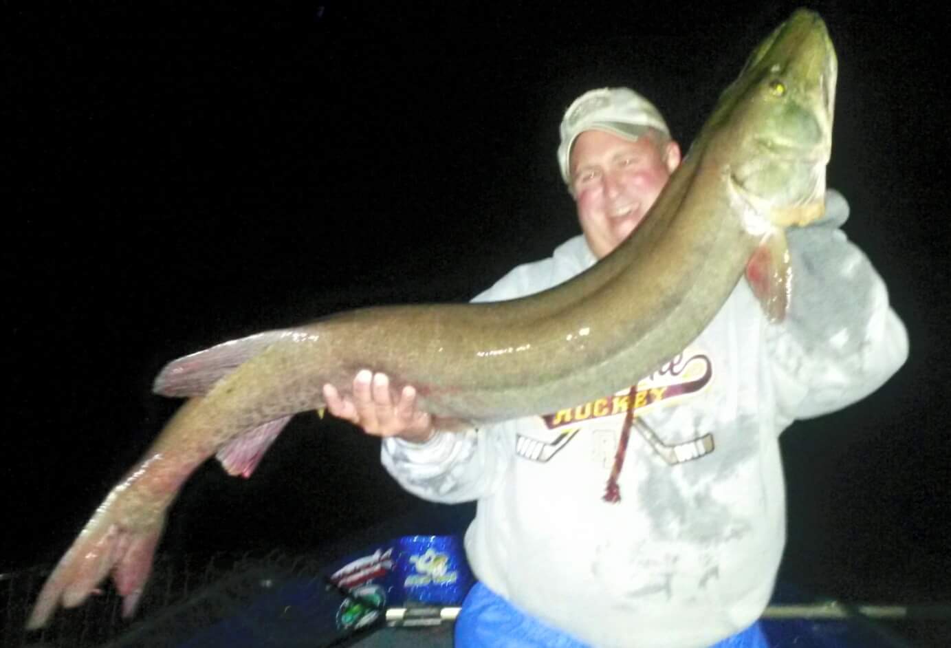 Guy smiling holding up a 55 inch muskie at night
