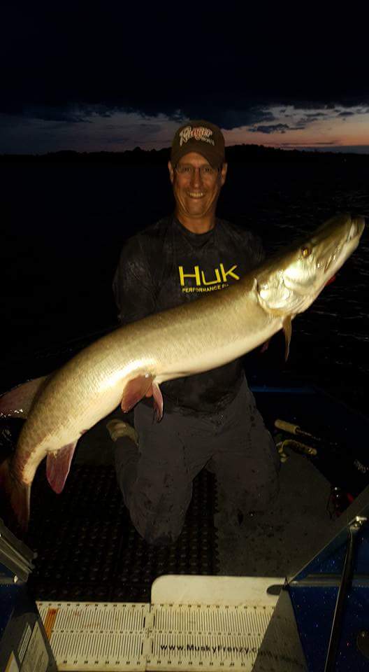 Gentleman holding up a large muskie fishing with Lake Vermilion Guide Service at night