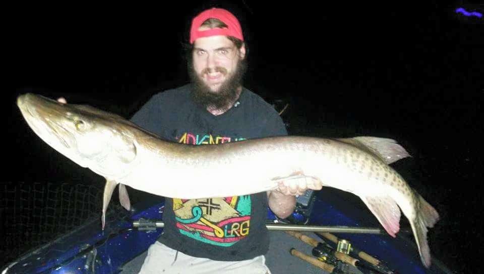 Guy in a redhat smiling and holding up a muskie with both hands he caught with Living Legends Guide Service